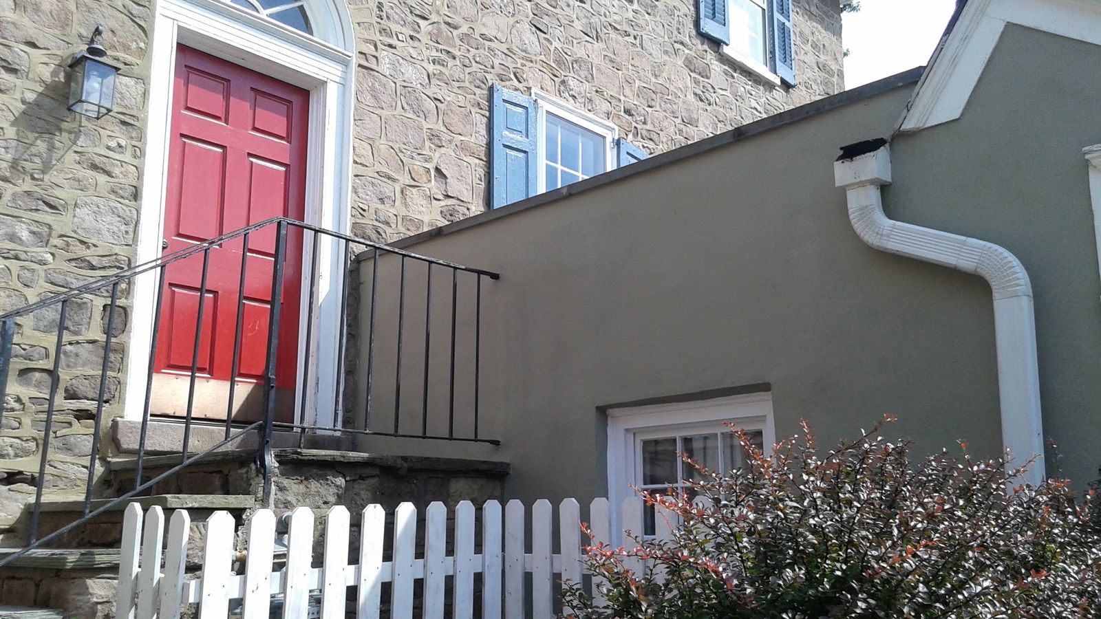 Home exterior with a red front door, stucco walls and white picket fence