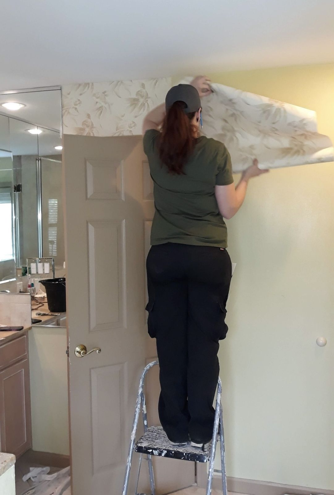 Installer on a ladder hanging wallpaper up to the ceiling